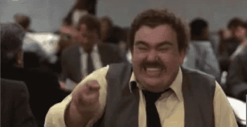 a man with a mustache is making a funny face while sitting in a crowd of people .