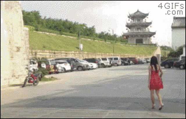 a woman in a red dress is walking down a street in front of a pagoda and a motorcycle