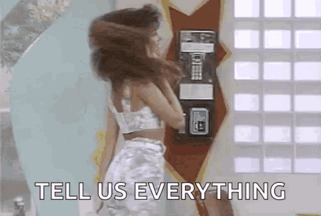 a woman is standing in front of a pay phone and talking on it .