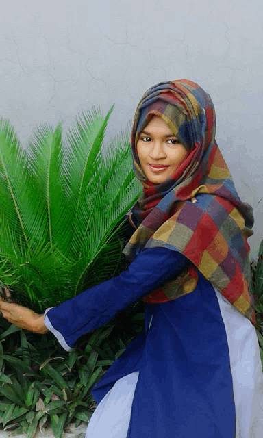 a woman wearing a colorful scarf is standing in front of a green plant