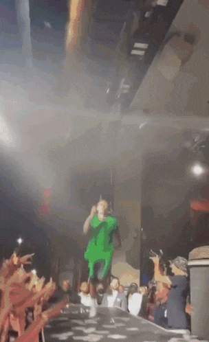 a man in a green shirt is jumping in the air on stage