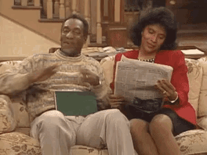 a man and woman are sitting on a couch reading a newspaper