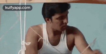 a man in a white tank top is sitting under a wooden structure .