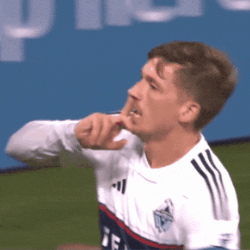 a soccer player wearing a white adidas jersey holds his finger to his mouth