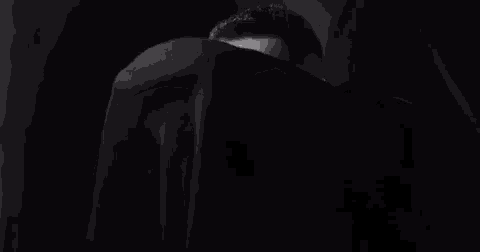 a black and white photo of a man peeking out from behind a black cloth .