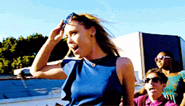 a woman in a blue top is screaming and sticking her tongue out while wearing sunglasses