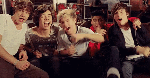 a group of young men are sitting on a couch and one of them is wearing an above us t-shirt