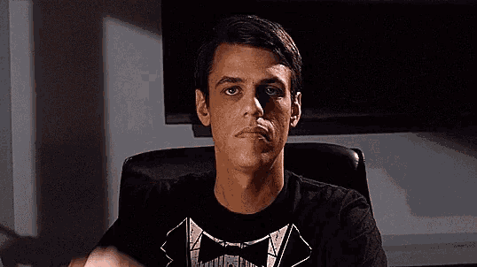 a man wearing a black shirt with a bow tie on it is sitting in a chair with his hands up .