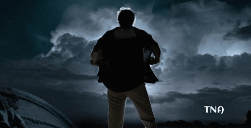 a man is standing in front of a cloudy sky with tna written on the bottom right