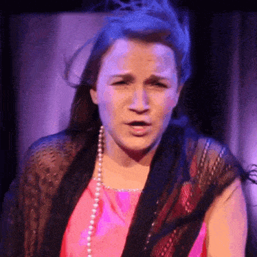 a woman in a pink top and pearls is making a face