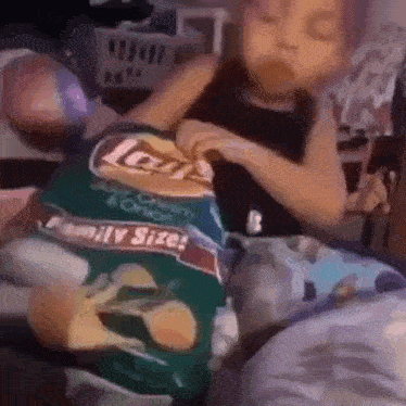 a little boy is eating a bag of lays chips .