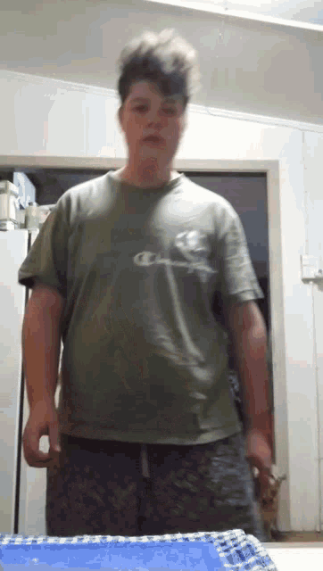 a young man wearing a green champion shirt stands in front of a door