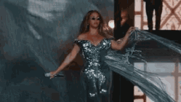 a woman in a silver dress is singing into a microphone on a stage