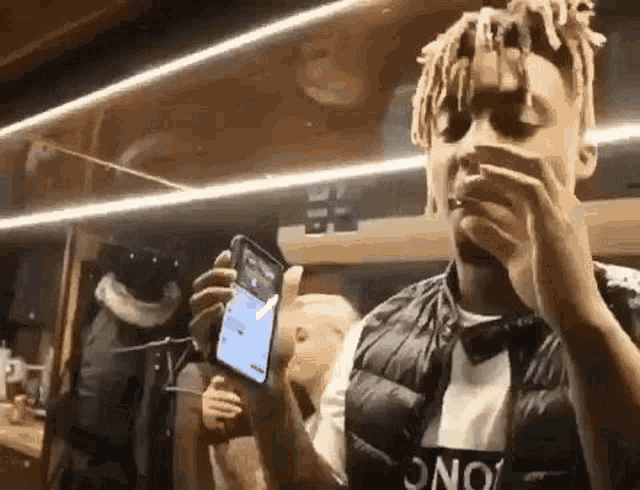 a man with dreadlocks is smoking a cigarette while holding a cell phone .