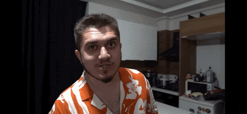 a man in a hawaiian shirt looks at the camera in a kitchen