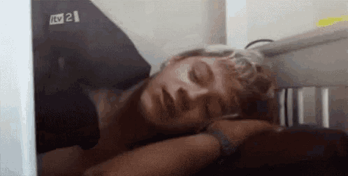 a man is sleeping in a bed with his eyes closed and a pillow on his head .