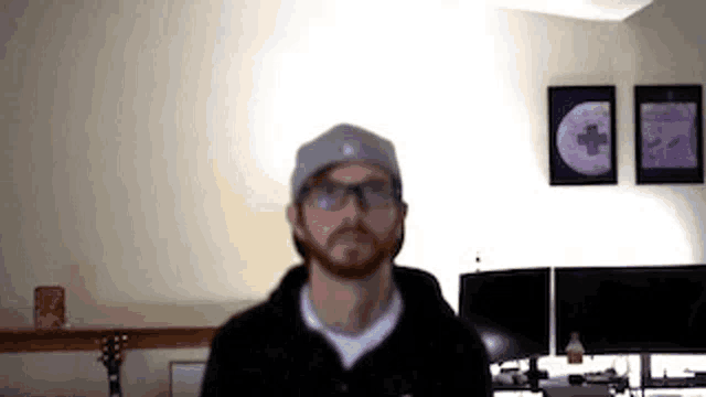 a man with a beard and glasses is wearing a hat and a hoodie in a living room .