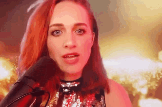 a woman with red hair is singing into a microphone in a sequined top