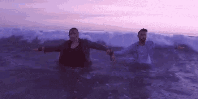 a man and a woman are in the ocean holding hands