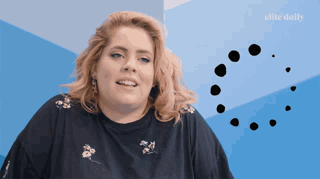 a woman is smiling in front of a blue wall with the elite daily logo