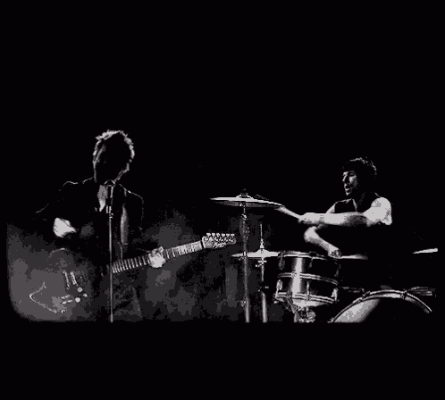 a black and white photo of a man playing drums in a dark room with smoke coming out of it .