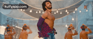 a man without a shirt is dancing with a group of men in a room .