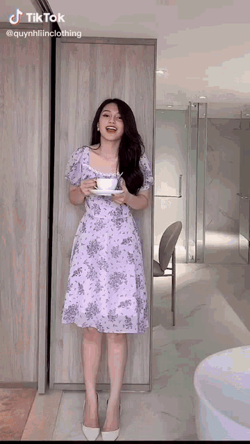 a woman in a purple dress is holding a cup of coffee in a bathroom .