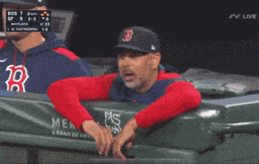 a man in a red sox hat is pointing at the scoreboard