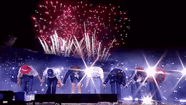 a group of people are standing on a stage with fireworks behind them .