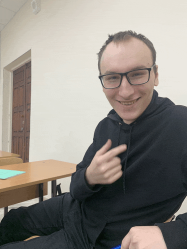 a man wearing glasses and a black hoodie is smiling and pointing