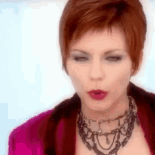a woman with short red hair is wearing a pink jacket and a necklace .