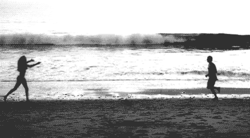 a black and white photo of a man and a woman running on a beach