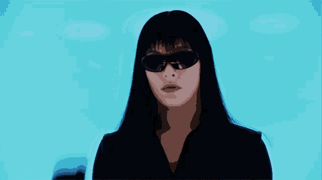 a woman wearing sunglasses and a black glove holds her hand up