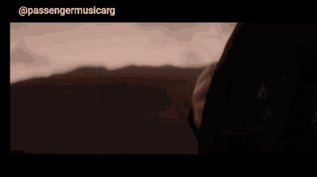a man with a beard looks out over a mountain range with passengermusicarg written below him