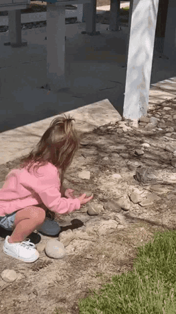 a little girl in a pink shirt is playing with rocks