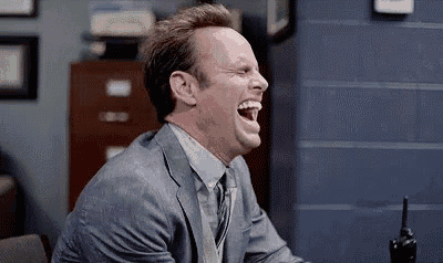 a man in a suit and tie is laughing with his mouth open .