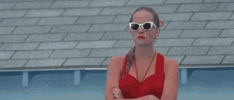 a woman wearing sunglasses and a red tank top is standing next to a swimming pool .