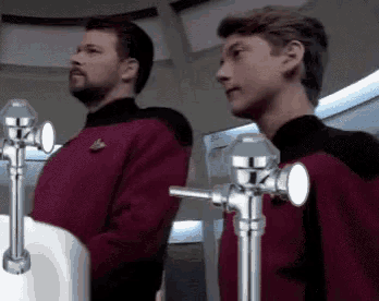 two men are standing in front of urinals in a public restroom .