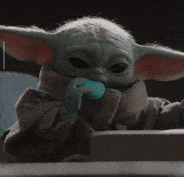 a baby yoda eating a blue macaroon in a dark room