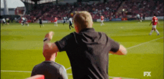 a man in a black shirt is watching a soccer game on a tv screen .