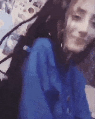 a girl with dreadlocks is wearing a blue hoodie and smiling .