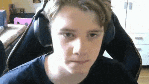 a young boy wearing headphones is sitting in a chair and making a face .