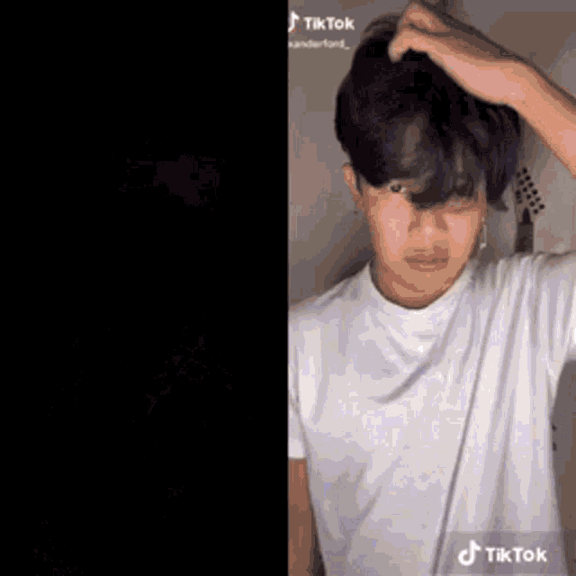 a man in a white t-shirt is scratching his head with his hand .