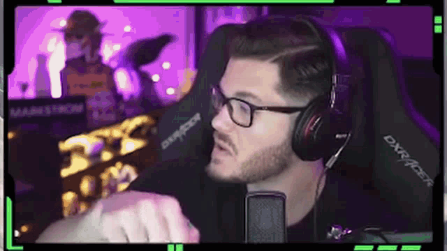 a man wearing glasses and headphones is sitting in front of a microphone in a purple room .