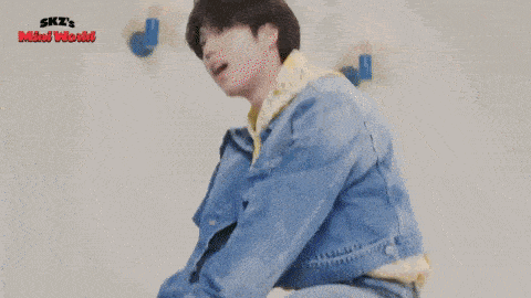 a young man in a blue denim jacket and jeans is laying on a yellow cushion .