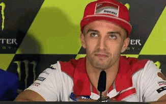 a man wearing a ducati hat is sitting in front of a monster energy sign