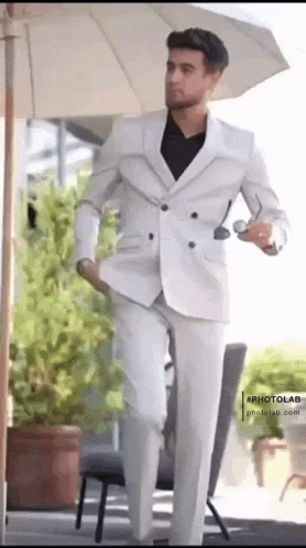 a man in a white suit is standing under a white umbrella
