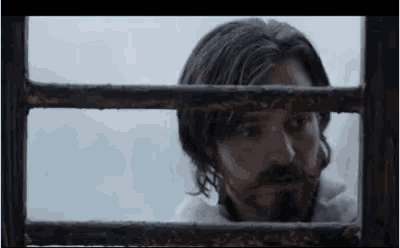 a man with a beard looks out of a window behind bars