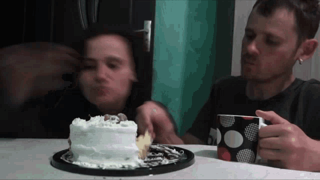 a man and woman sit at a table with a cake and a cup of coffee
