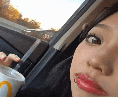 a woman sitting in a car with a mcdonald 's cup in her hand